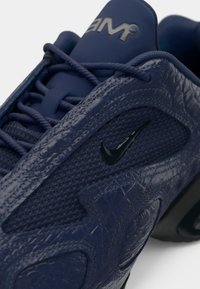 Gros plan d'une chaussure Nike bleu marine avec dessus texturé, logo Nike noir et lacets visibles sur le dessus et sur le côté de la chaussure.