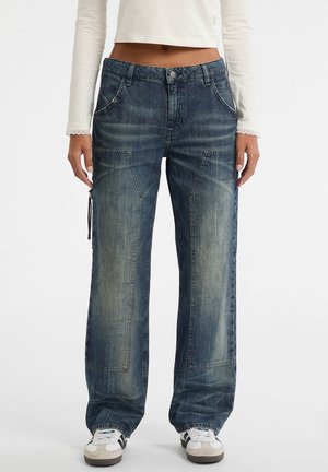 Wijdvallende blauwe denim jeans met een vervaagde afwerking, voorzien van voorzakken, stikseldetails en een rits aan de zijkant. Gekoppeld met sneakers.