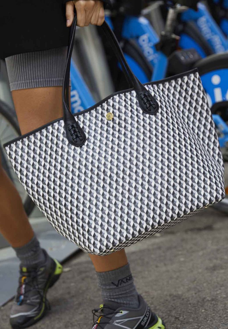 Black and white geometric patterned tote bag with black handles and gold accent. Features a triangular design and spacious rectangular shape.