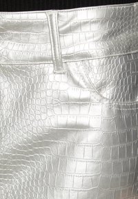 Silverfärgad faux läderkjol med en texturerad krokodilmönster, med midjeband och sidofickor. Slät, blänkande yta.