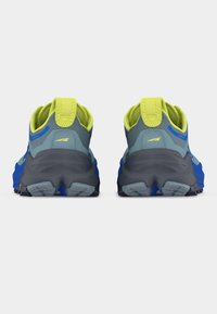 Ζευγάρι αθλητικών παπουτσιών σε μπλε και γκρι χρώμα με κίτρινες αποχρώσεις, από πίσω, που δείχνουν χοντρές σόλες και θηλιές έλξης σε λευκό φόντο.