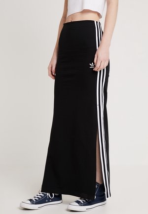 Zwarte maxi rok van polyester met witte zijstrepen. Heeft een hoge split en een klein Adidas-logo aan de linkerkant. Gecombineerd met blauwe sneakers.