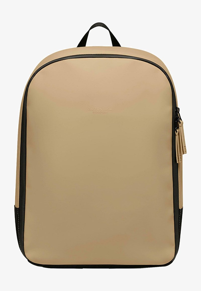 Sac à dos beige avec une finition lisse et mate. Comprend une fermeture éclair noire sur le côté, une poignée supérieure et un logo en relief. Forme rectangulaire. Design minimaliste.