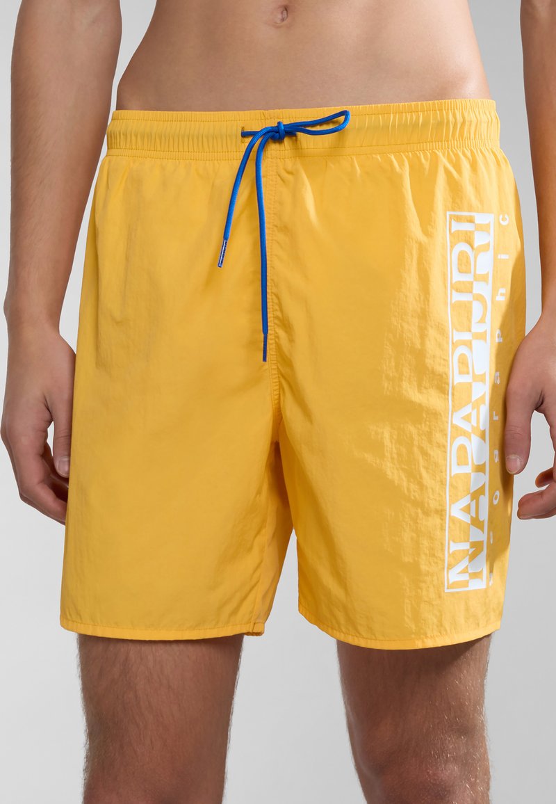 Gele zwembroek van lichtgewicht stof, met een blauwe trekkoord, zijzakken en een groot wit logo aan de linkerzijde.