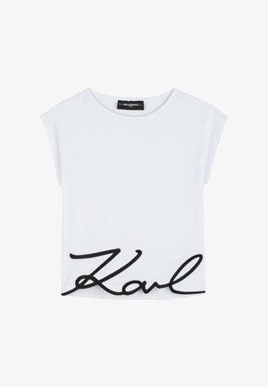 Camiseta blanca de manga corta con cuello redondo amplio y gran texto cursivo negro "Karl" bordado cerca del dobladillo inferior.