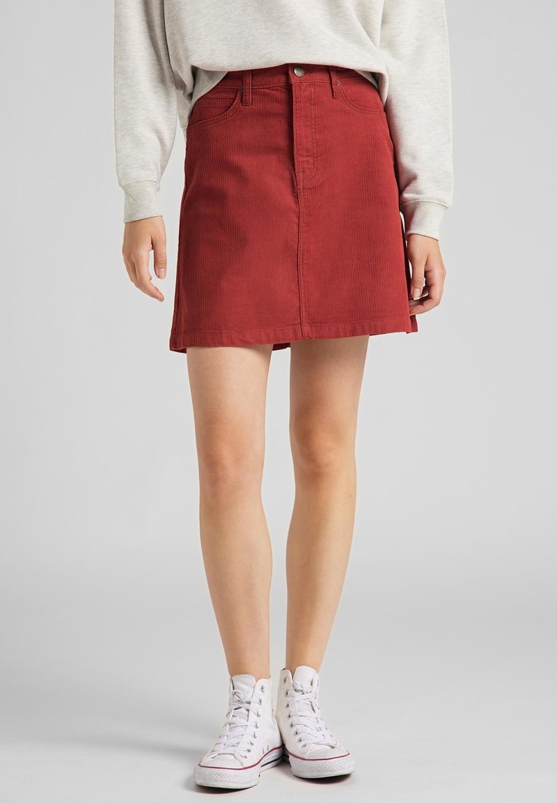 Falda de pana roja con bolsillos frontales, un cierre de botones y un dobladillo recto. Combinada con zapatillas altas blancas.