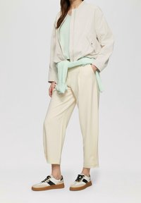 Light beige bomber jacket, mint green knit top, cream pants, and multicolored sneakers. Features zip closure and pockets.