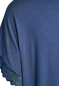 Tuva zilas auduma ar mežģīņu apdari, kuras rakstā redzams chevron raksts uz drēbes piedurknes malas.