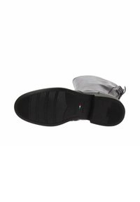Suela de goma negra de una bota con surcos horizontales y patrones texturizados. La parte superior está hecha de cuero gris con una silueta redondeada.