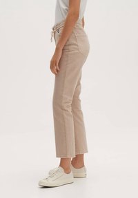 Vaqueros de talle alto en color beige con pierna recta, hechos de denim, con cintura ajustable y dos bolsillos traseros, combinados con zapatillas blancas.