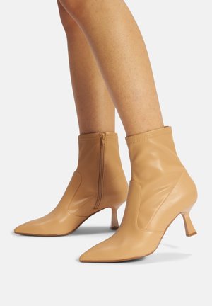 Botas de tobillo de cuero color marrón claro con punta afilada, diseño a la altura del tobillo y cierre lateral. Presentan un tacón delgado y geométrico que añade elegancia.