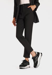 Pantaloni neri su misura con una vestibilità slim e tasche laterali, abbinati a sneakers nere e argentate con una spessa suola bianca.