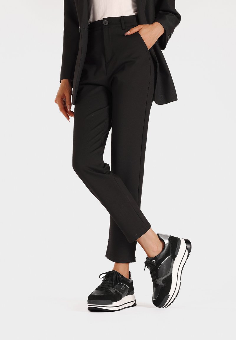 Pantaloni neri su misura con una vestibilità slim e tasche laterali, abbinati a sneakers nere e argentate con una spessa suola bianca.