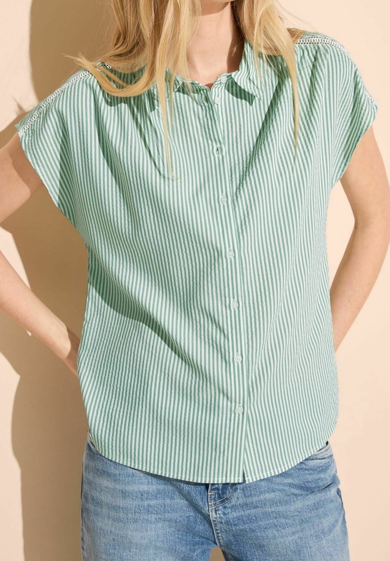 Chemise à manches courtes à rayures vertes et blanches avec une coupe décontractée, présentant un ourlet arrondi et un détail texturé aux épaules.