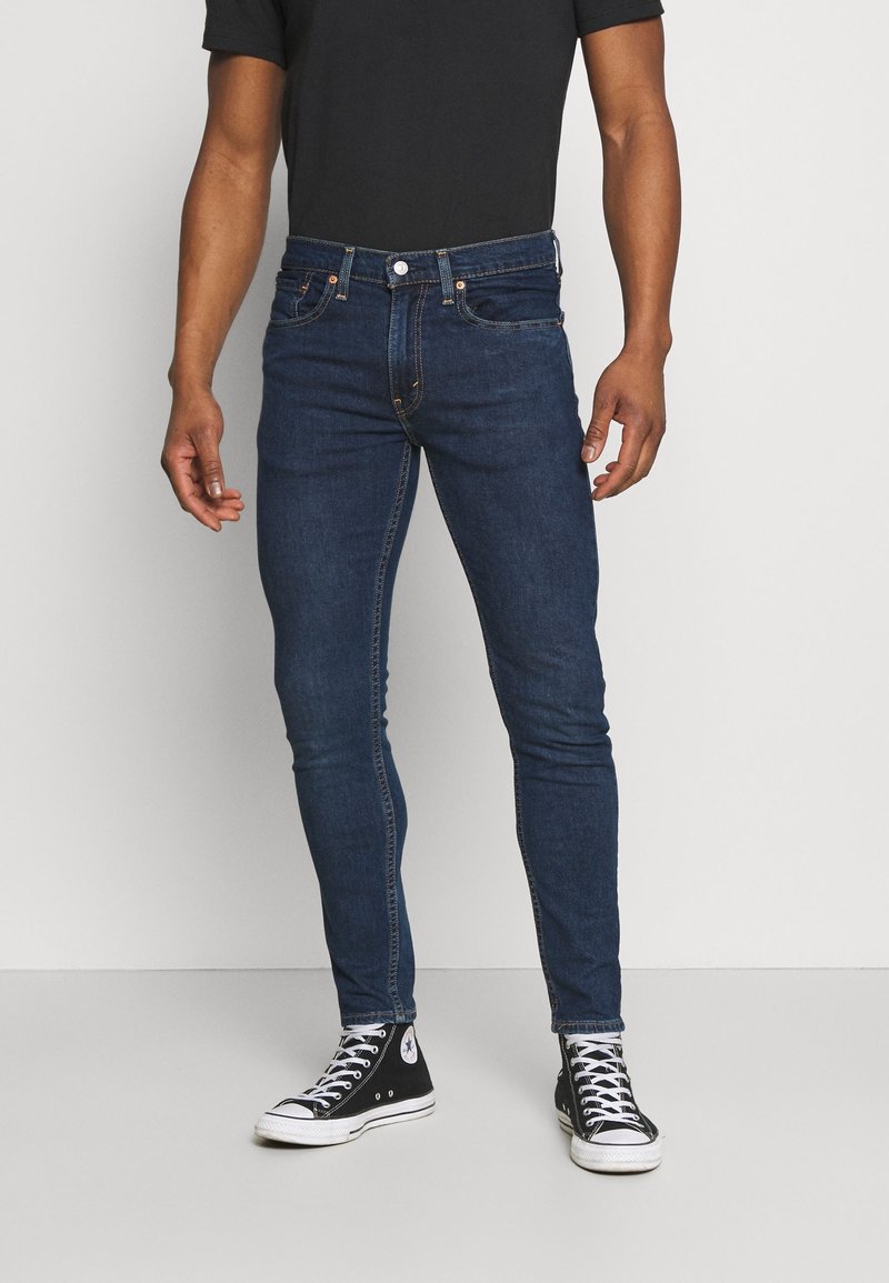Skinny-fit dark blue jeans made of denim, featuring five pockets, subtle stitching, and a classic button and zipper fly closure.