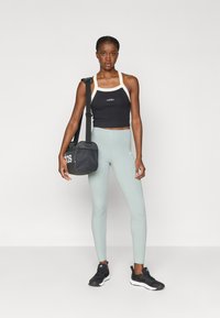 Črn športni top s svetlimi naramnicami, svetlozeleni leggins, črne športne čevlje in majhna črna torbica čez ramo.