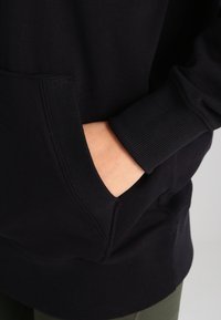 Felpa nera con cappuccio caratterizzata da una grande tasca frontale, polsini e bordo a coste. Tessuto morbido con una texture liscia e una vestibilità casual.