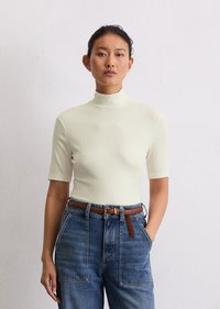 Vaalean kreeminvärinen, ribbiluinen turtleneck-toppi lyhythihaisena, yhdistettynä vyötärön korkeisiin, rentoihin sinisiin farkkuihin ja ruskeaan nahkavyöhön.