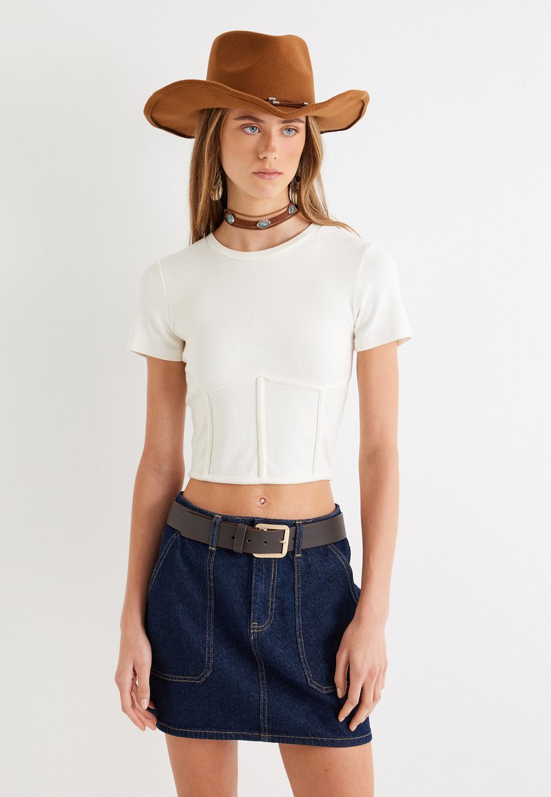 Hvid cropped top med korte ærmer, mørkeblå denimnederdel, grå bælte, brun filt hat og en choker med turkise accenter.