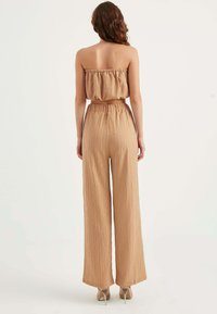 Beżowy top bez ramiączek z elastycznym falbanem przy dekolcie, połączony z szerokimi, teksturowanymi spodniami na gumce.