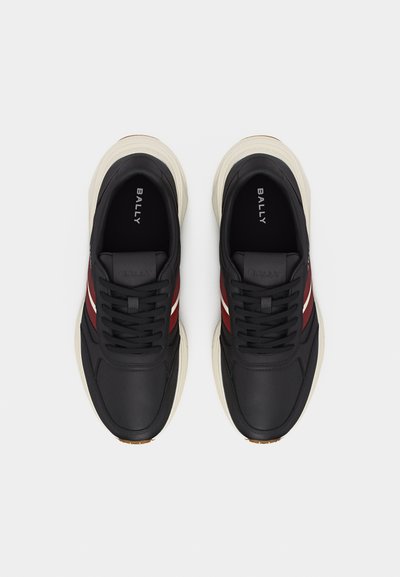Paire de baskets noires Bally avec semelles blanches et bandes latérales rouges, vues de dessus sur fond blanc.