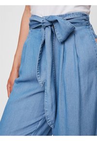 Ljust blå denimbyxor med bred byxben-design, försedda med en knytning i midjan och en texturerad tyg. Fickor ger strukturen till stilen.