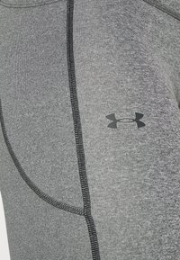 Szare legginsy sportowe o gładkiej teksturze, z czarnymi akcentami szycia i logo Under Armour po boku.