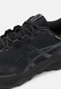 Scarpa da corsa nera con tomaia texturizzata, pannelli in rete e logo tonale. Presenta il marchio Gore-Tex e una suola in gomma distintiva.