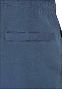 Tengerés kék pamut jogger nadrág texturált derékkal, puha anyaggal és egy kis hátsó zsebbel, amely vízszintes nyílással rendelkezik.