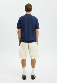 Mornarski polo majica s kratkimi rokavi in ovratnikom, v kombinaciji s kremnimi hlačami do kolen in črnimi čevlji. Enostaven dizajn z minimalnimi detajli.