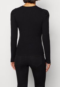 Maglietta nera a maniche lunghe con design aderente, caratterizzata da sottili accenti spalle a sbuffo e scollo tondo. Tessuto liscio su tutta la superficie.