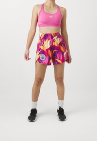 Rosa sportbh och färgglada shorts med blommönster och en blå emblem. Shortsen har ett elastiskt midjeband och är tillverkade av lättviktig tyg.