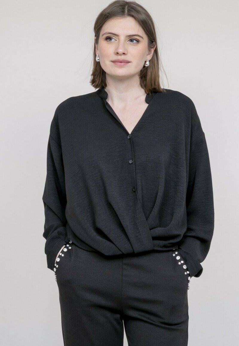 Chemise noire, ample, avec un décolleté en V et un devant à boutons. Texture douce, manches longues, associée à un pantalon noir assorti avec des boutons décoratifs.