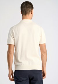 Krämbelädd kortärmad pikétröja med en slät yta, ribbad krage och fåll, samt subtila detaljer på axlarna, i kombination med mörka byxor.