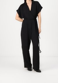 Combinaison noire à manches courtes, décolleté en V et ceinture détaillée. Fabriquée en tissu léger, avec une coupe décontractée et des jambes droites.