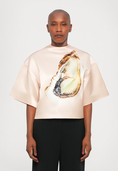 Cropped satin top in soft peach with a large oyster shell print. Features wide sleeves and a high neckline. Paired with black trousers.