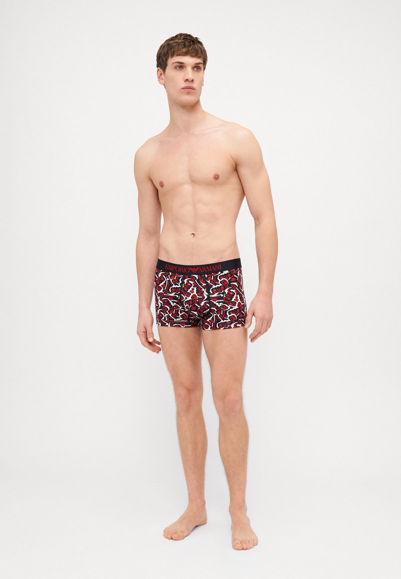 Un maillot de bain à motifs rouge et noir avec une coupe ajustée, doté d'une ceinture noire avec un détail de logo et une texture lisse.