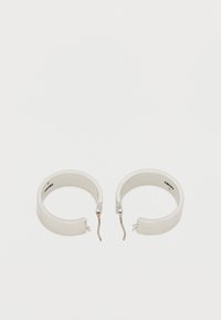 Beli kovinski uhani v obliki obroča z gladkim zaključkom. Imajo preprost odprt dizajn in minimalistično srebrno zaponko. Elegantno in moderno.