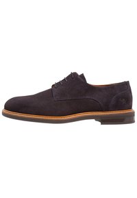 Chaussure Oxford en daim bleu foncé avec une texture lisse, un bout rond et une semelle en cuir beige. Dispose de cinq œillets pour les lacets.