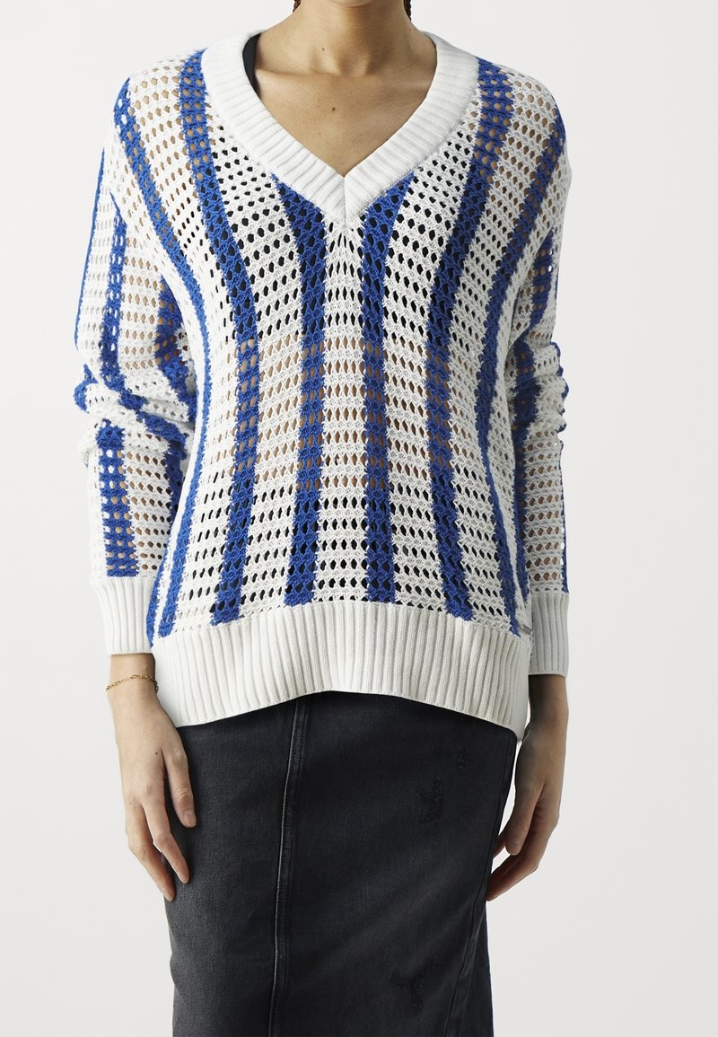 Valkoinen neulepaita, jossa on sinisiä raitoja, v-kuviointi sekä ribbireunat hihoissa ja helmassa. Sisältää avoimen kudontamallin. Yhdistetty mustan hameen kanssa.