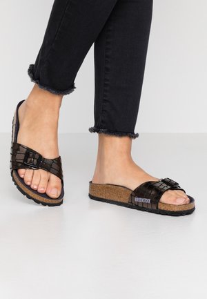 Stopy w czarnych teksturowanych sandałach Birkenstock typu slide z korkowymi podeszwami i regulowanymi paskami z klamrą, zestawione z czarnymi dżinsami z postrzępionym dołem.