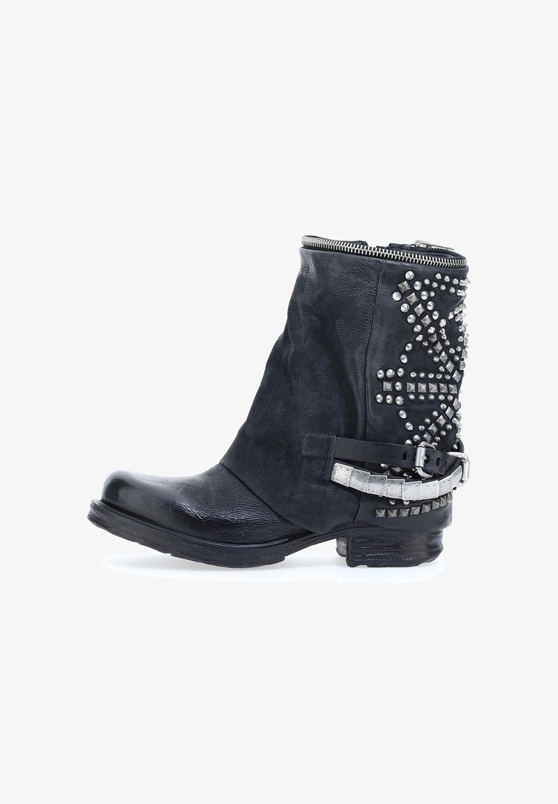 Bota de cuero negra a la altura del tobillo con un acabado texturizado, tachuelas plateadas en el costado y una correa de hebilla metálica. Cuenta con un cierre de cremallera en la parte superior.