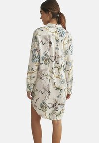 Robe chemise blanche à manches longues, ornée d'un motif floral et de grues en bleu, vert et marron. Tissu lisse, ourlet légèrement arrondi.