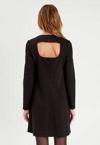 Vestido negro de manga larga con corte cuadrado en la espalda, textura suave y diseño ajustado, que termina justo por encima de la rodilla.