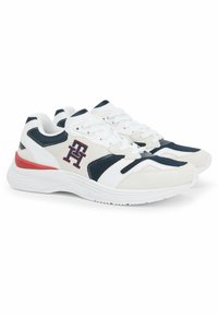 Zapatillas deportivas blancas con acentos en azul marino, paneles de malla y una pieza en rojo en el talón. Presentan un logotipo prominente en el costado y detalles texturizados.
