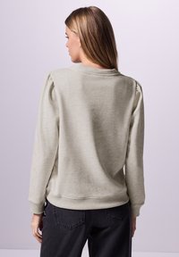 Felpa grigio chiaro con finitura testurizzata, maniche a costine e vestibilità rilassata. Presenta spalle leggermente imbottite e scollatura a girocollo.