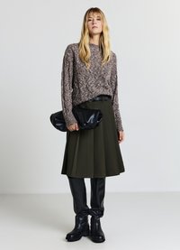 Knit sweater in light brown with textured pattern, paired with dark green pleated skirt, black faux leather pants, and black ankle boots.