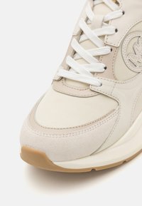 Baskets beige clair avec un mélange de cuir lisse et de daim, accents texturés, lacets blancs et semelle en caoutchouc beige.