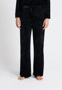 Pantalones de terciopelo negro con una textura suave, diseño de pierna ancha y una cintura elástica con cordón. Sin patrones ni acentos visibles.