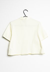 Polo z krótkim rękawem w jasnym żółtym kolorze wykonany z bawełny. Posiada klasyczny kołnierzyk oraz luźny krój z widocznym przeszyciem na końcach.